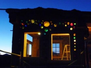 cordwood house at night with recycled glass windows shining